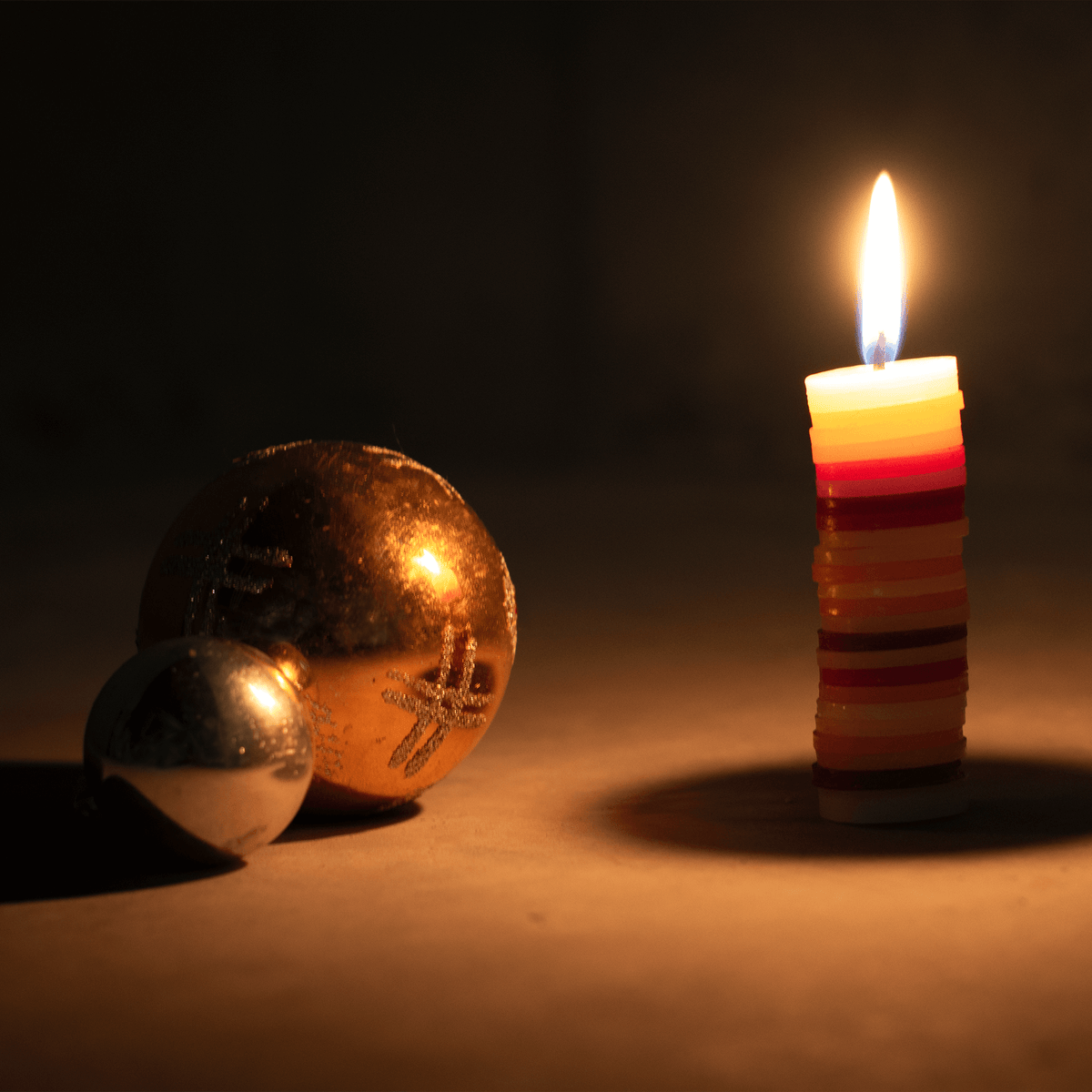 Brennende Kerze neben Christbaumkugeln